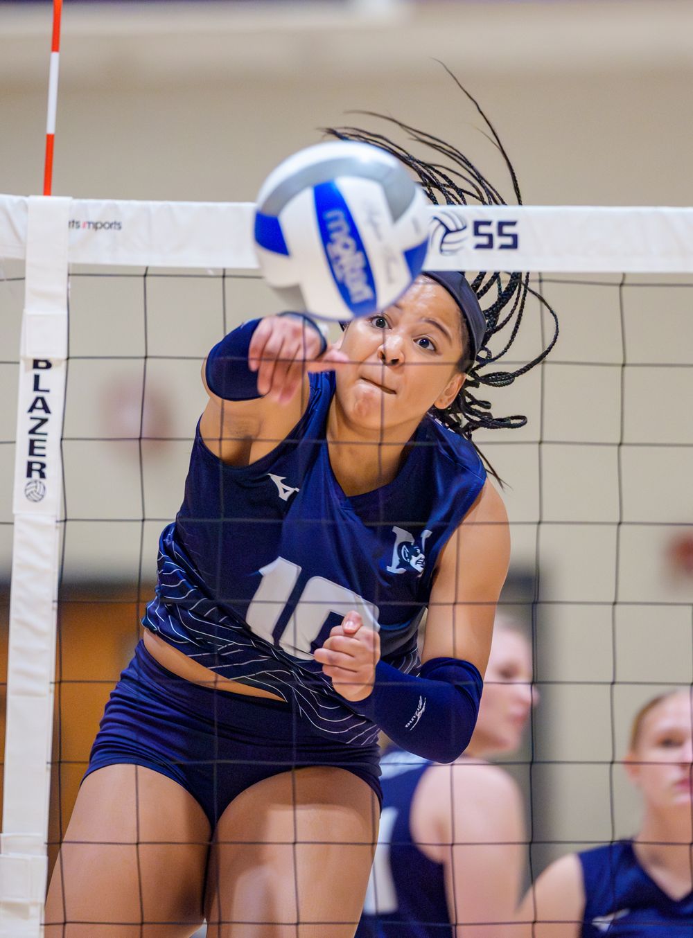 Player in navy uniform hits volleyball against net during competitive match.