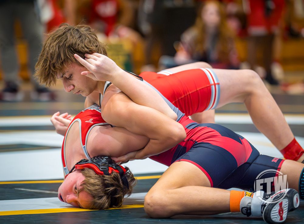 Two wrestlers competing intensely on a mat during a wrestling match.