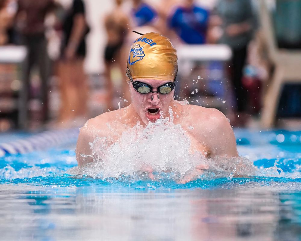 Swimmer performing butterfly stroke with water splashing during competitive swim meet.