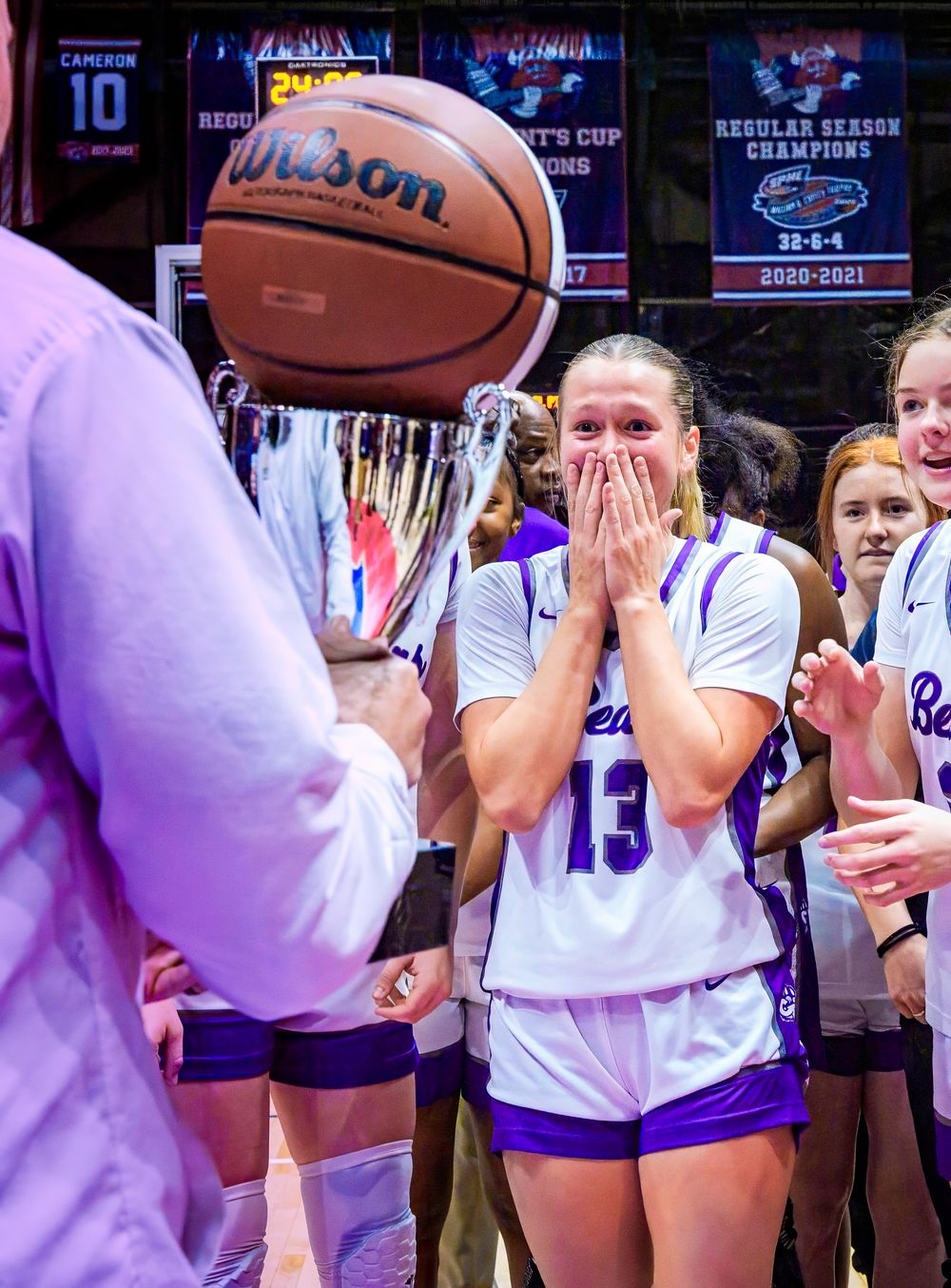 Basketball player in white jersey #13 shows emotional reaction during team championship celebration in arena.