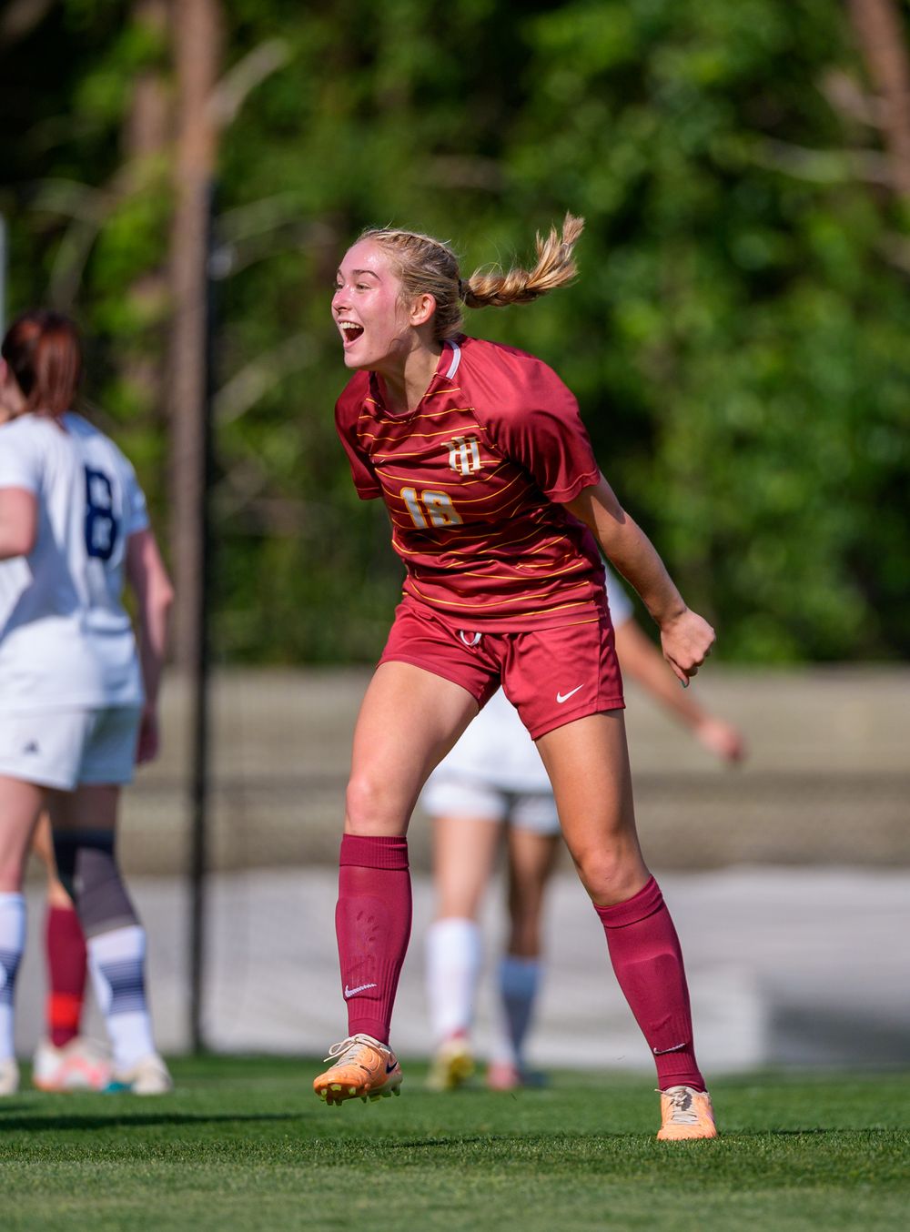 Player in maroon uniform celebrates passionately during soccer match on outdoor field.