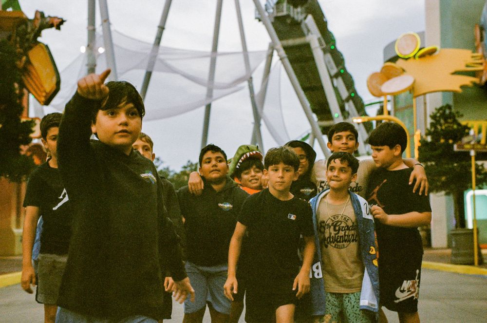 A group of children in black shirts walking together on a street with an industrial backdrop in warm vintage film tones.