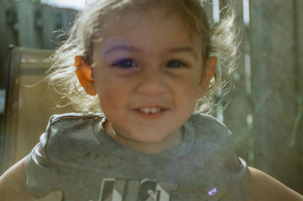 Close-up portrait of a small child wearing a gray t-shirt with bright sunlight creating a backlit glow effect.