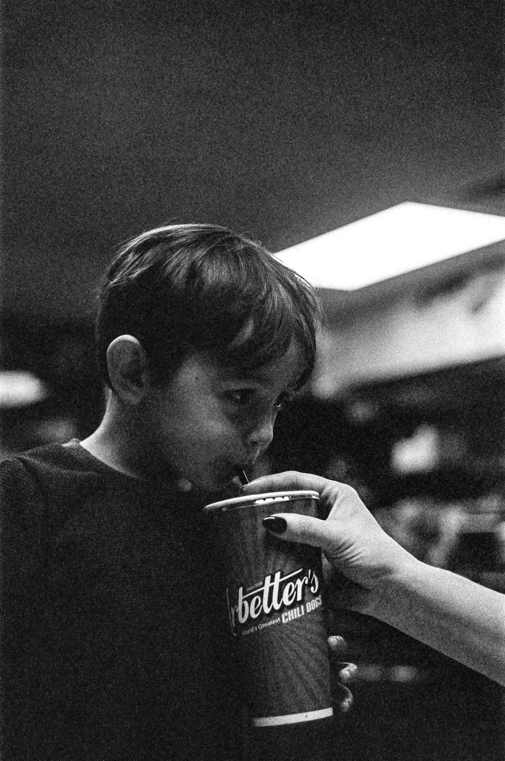 A black and white photograph of someone drinking from a paper cup in a dimly lit setting.