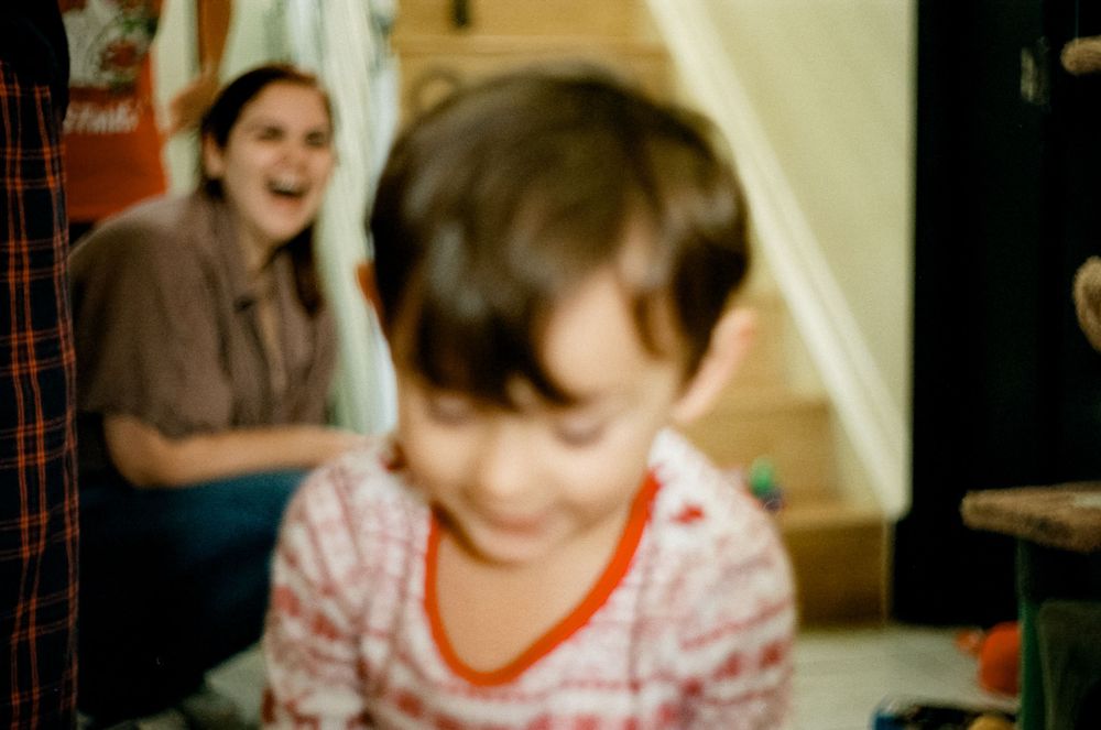 A blurry vintage photograph captures a child wearing a pink and white striped shirt with orange trim in an indoor setting.