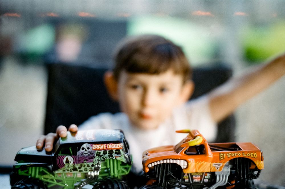 Selective focus shot of orange and green toy monster trucks with blurred background.