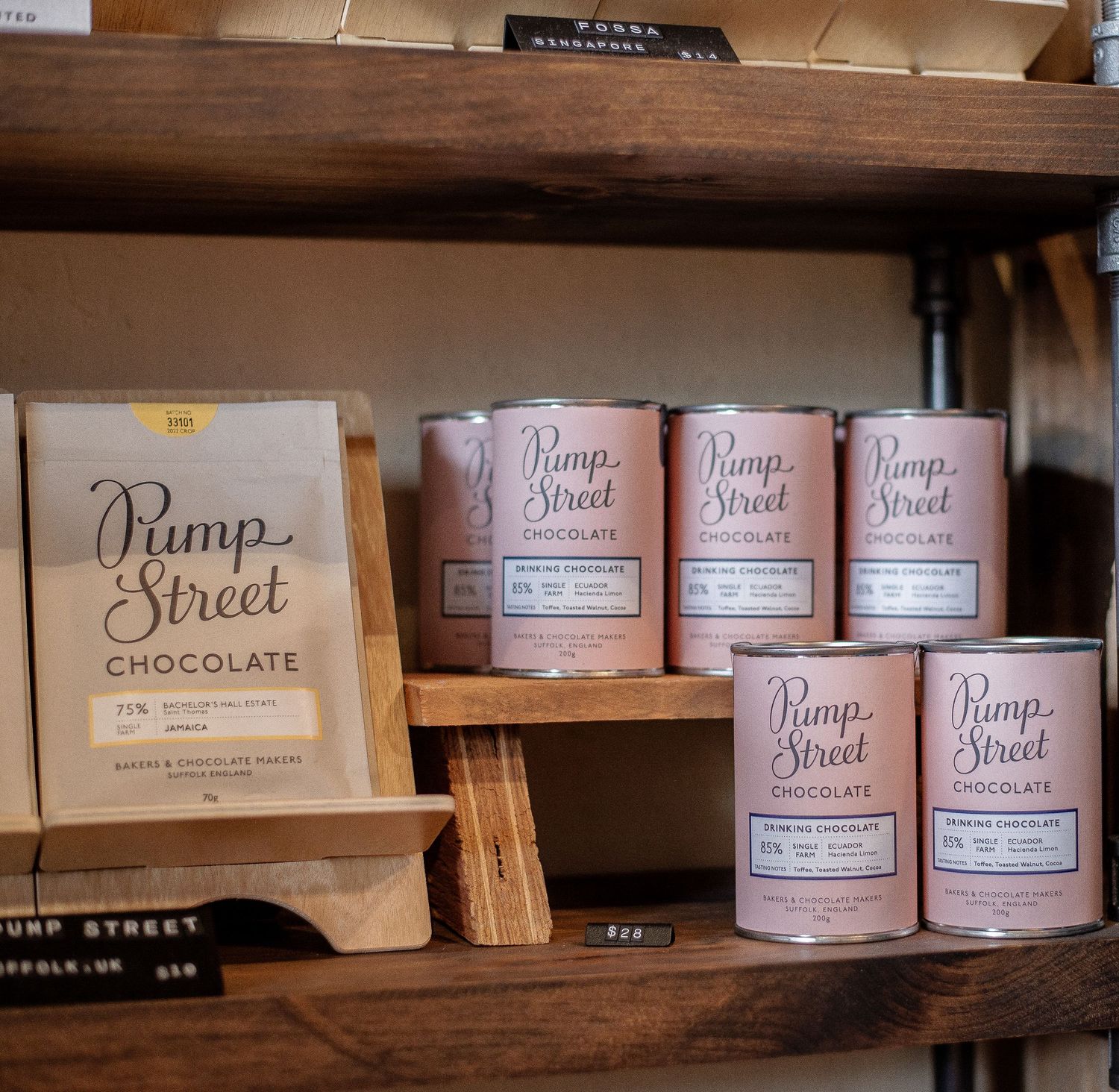 Pump Street Chocolate bars and pink cylindrical tins displayed on wooden shelves in a retail store.