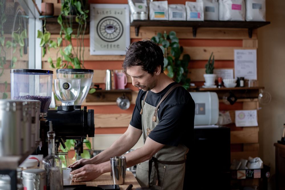 Barista in apron operates espresso grinder in a cozy wood-paneled coffee shop.