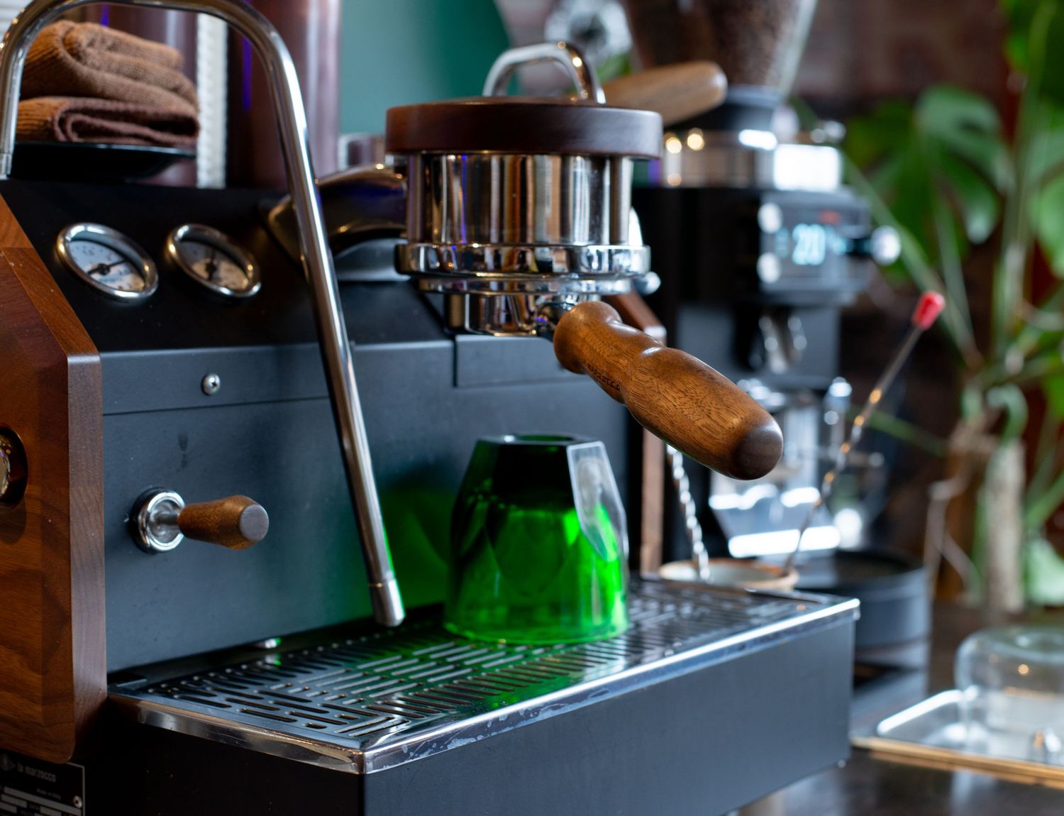 Close-up of a sleek espresso machine with wooden handles and a green steaming pitcher in a cafe.