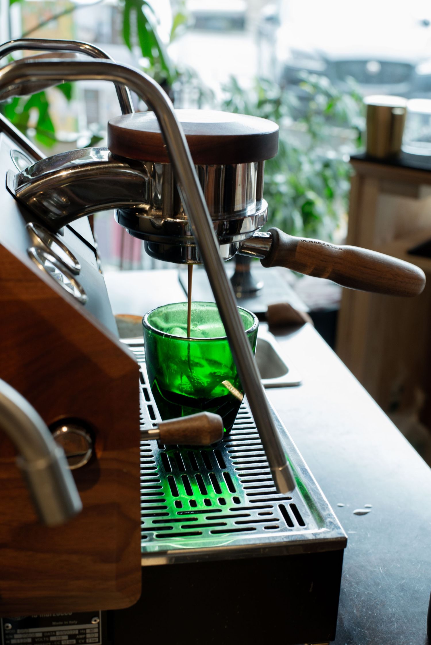 Espresso machine brewing coffee into a green glass cup in a bright cafe setting.