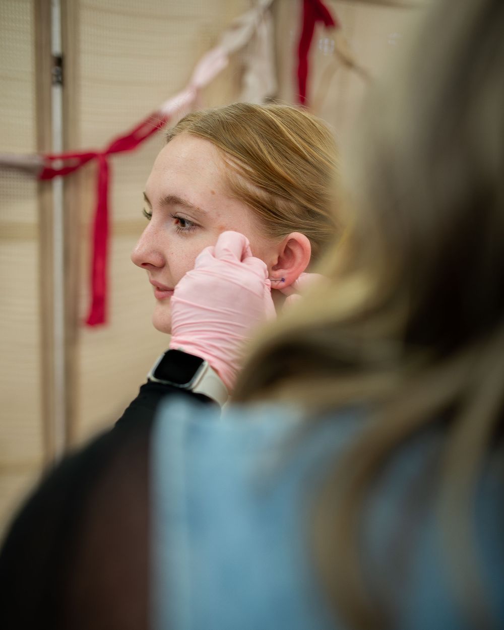 Close-up of professional piercer in pink gloves examining clients ear at an indoor piercing station.