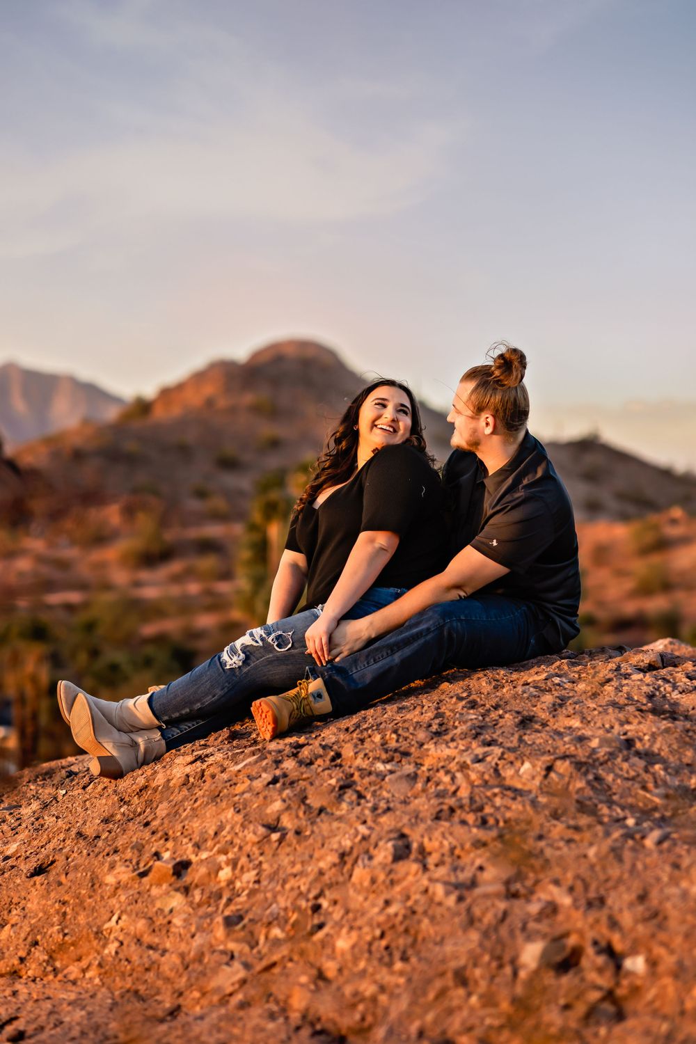 Two friends sitting on rocky terrain enjoying sunset in desert mountain landscape.