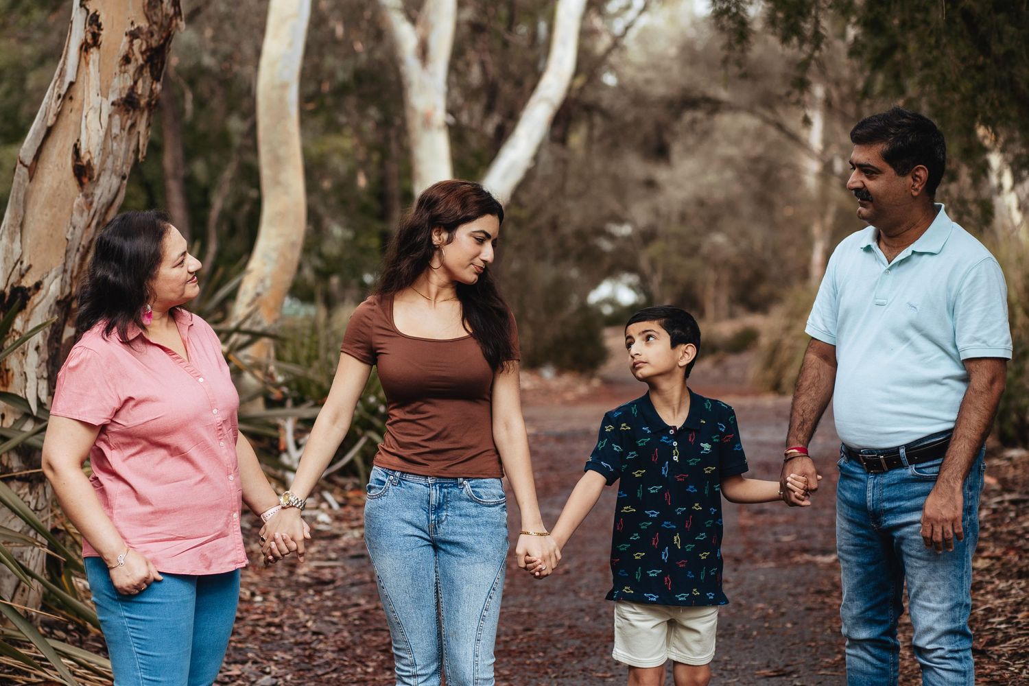 Family holding hands while walking together on a forest trail among eucalyptus trees on a sunny day.