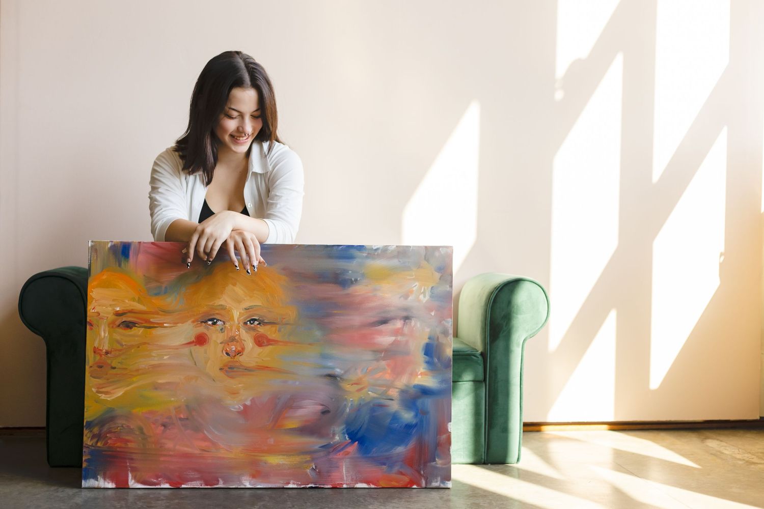 Artist sitting on floor next to vibrant abstract painting featuring warm sunset colors and blue tones.