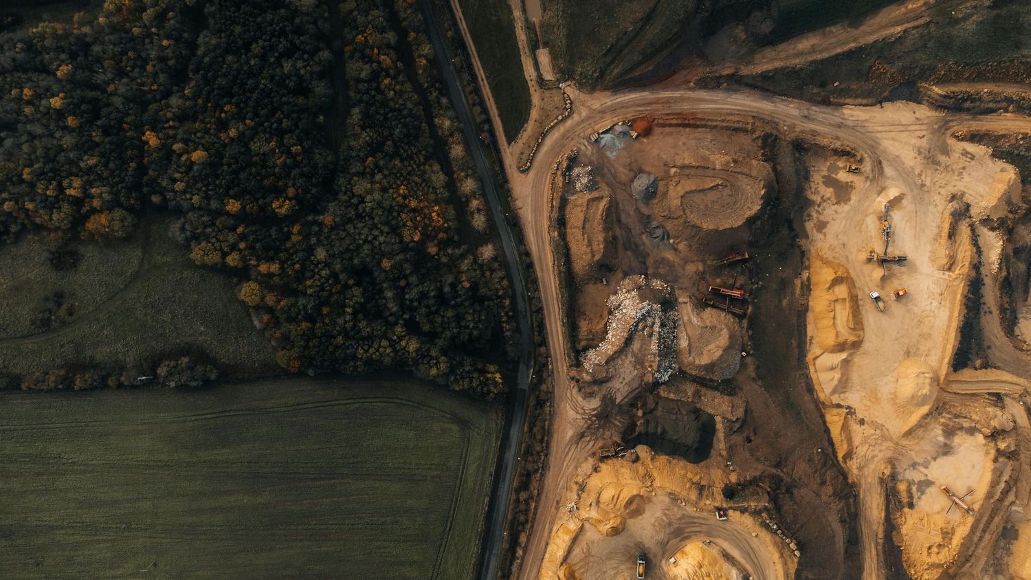 Aerial view of an open pit mining operation with earthen excavation visible against green forest.