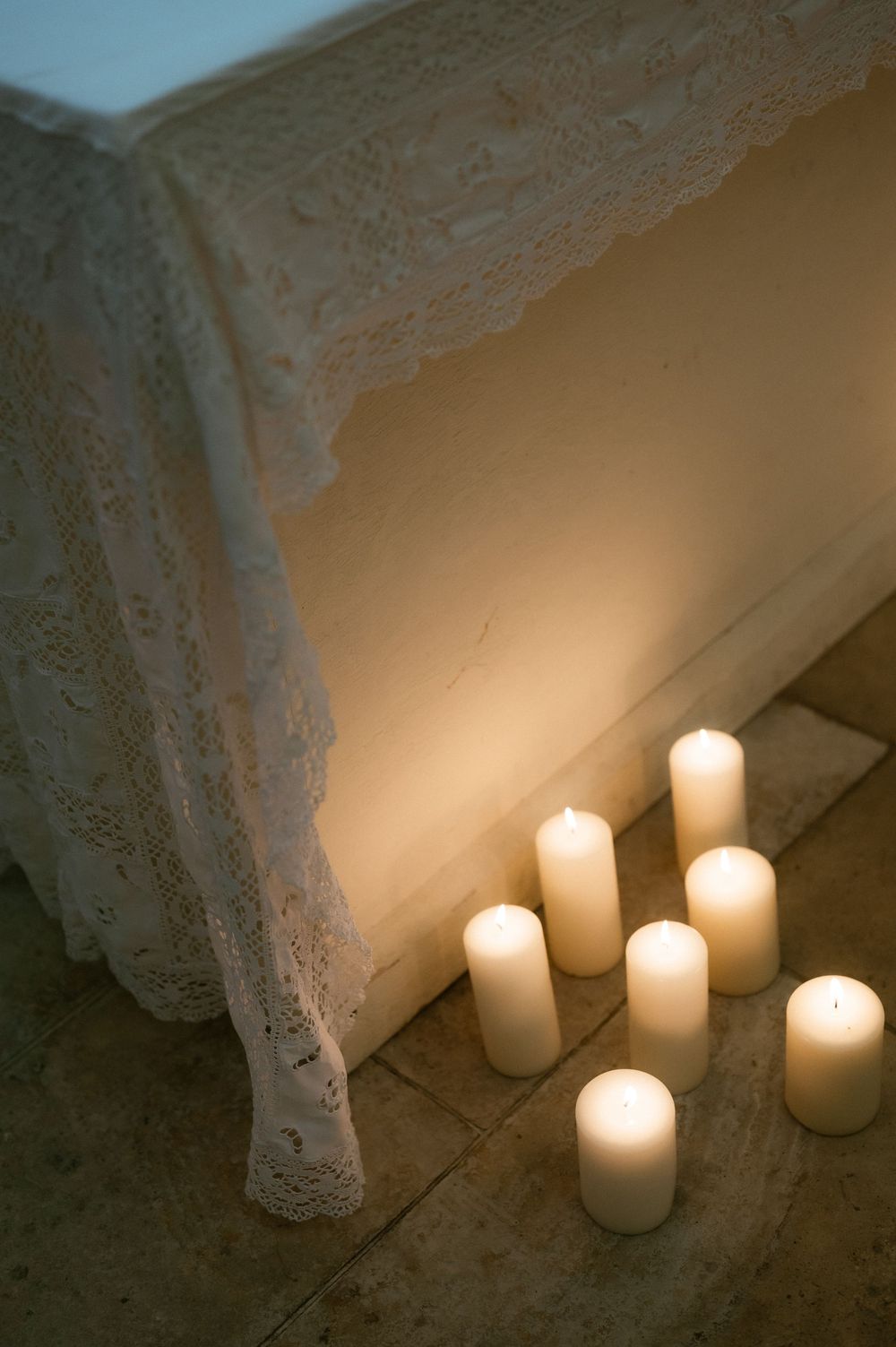 Row of white candles with lace decorations glowing softly against a neutral background.