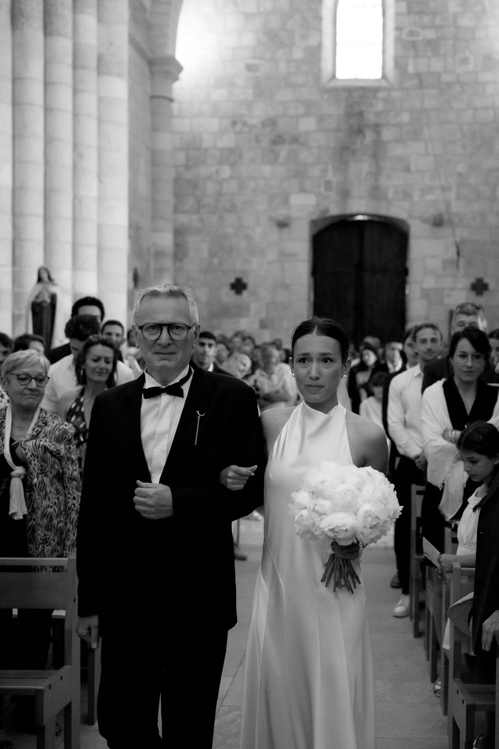 Wedding ceremony in a traditional stone church with guests seated in wooden pews during a solemn moment.