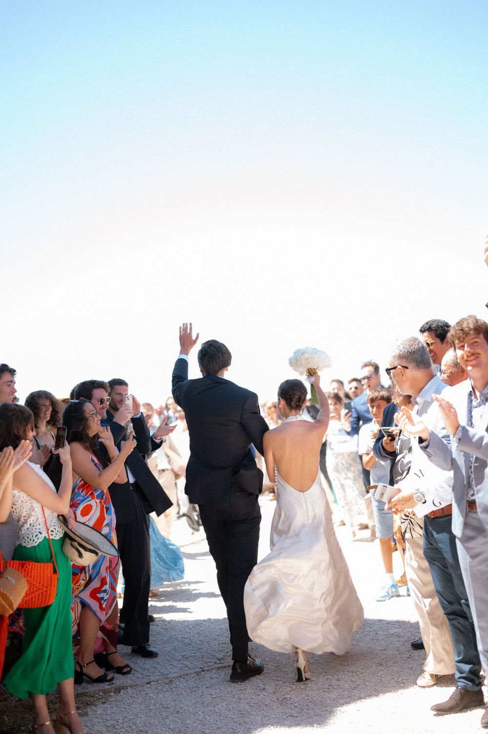 Wedding celebration on a sunny beach with guests dancing and celebrating in formal attire.