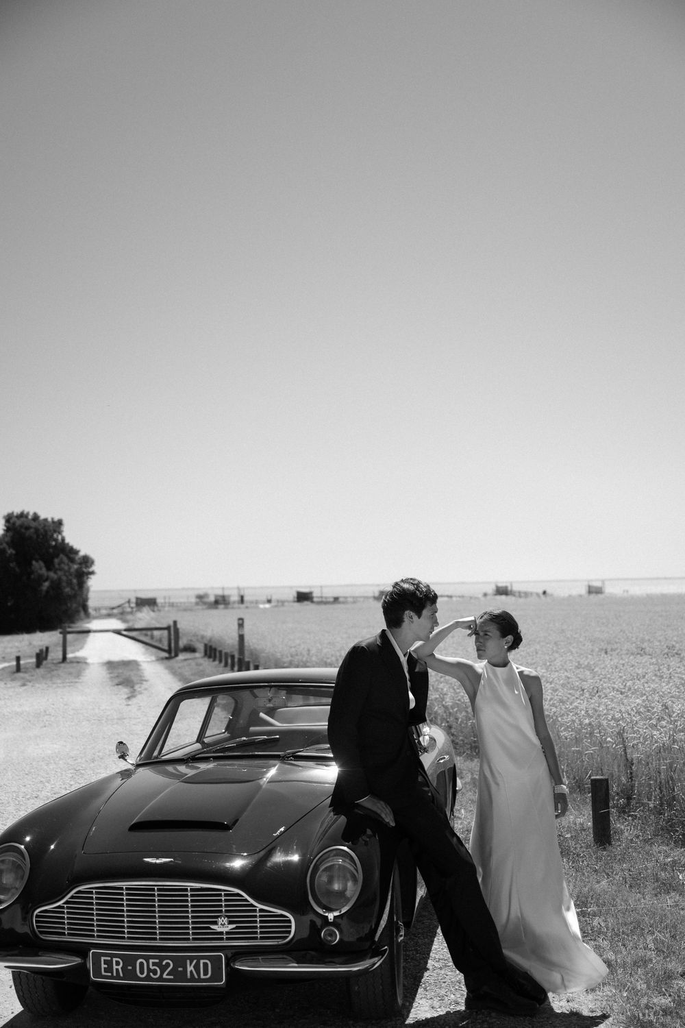 Classic black Aston Martin car parked in a countryside field on a wedding day.