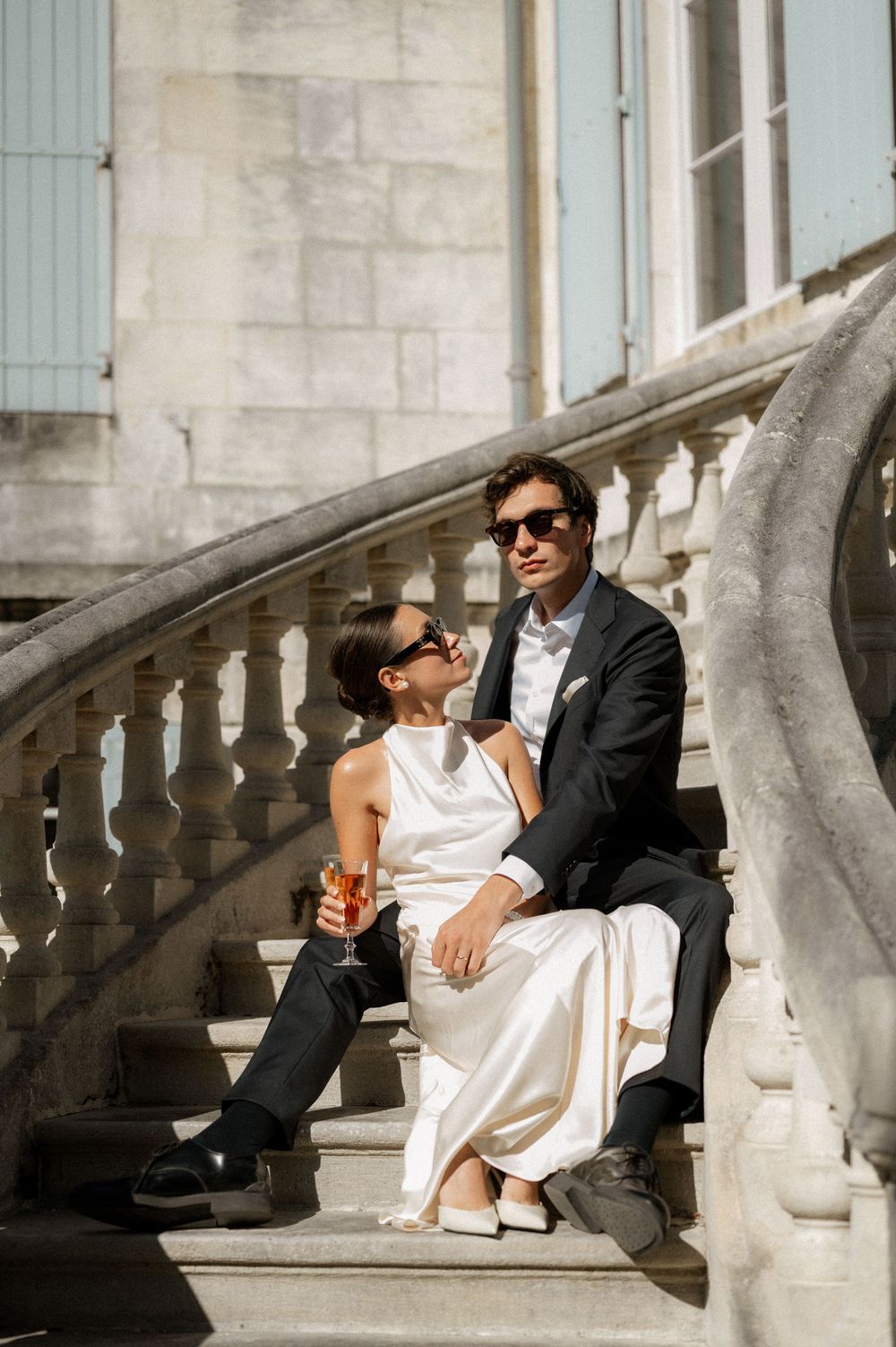 Couple relaxing on elegant stone steps of a historic building with blue shutters.