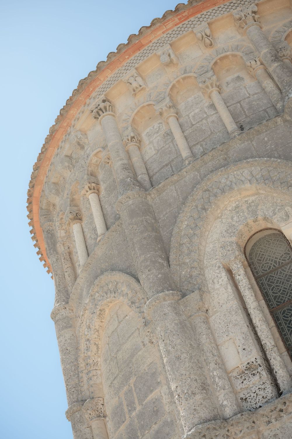 Architectural detail of a curved stone church wall with Romanesque arched windows and decorative moldings in warm sunlight.
