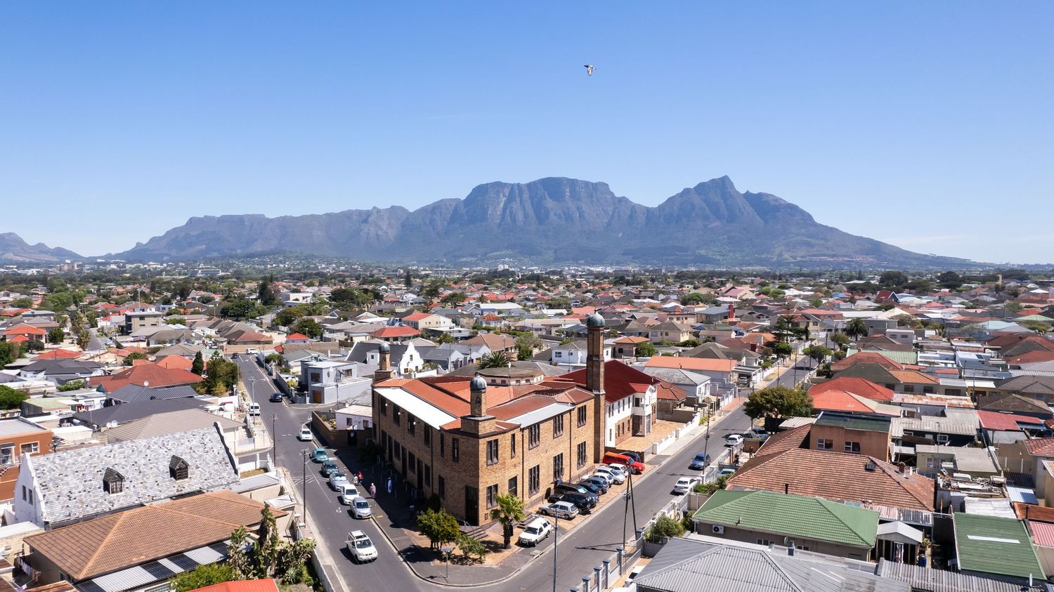 Panoramic view of a residential area with mountains looming in the background under blue skies.