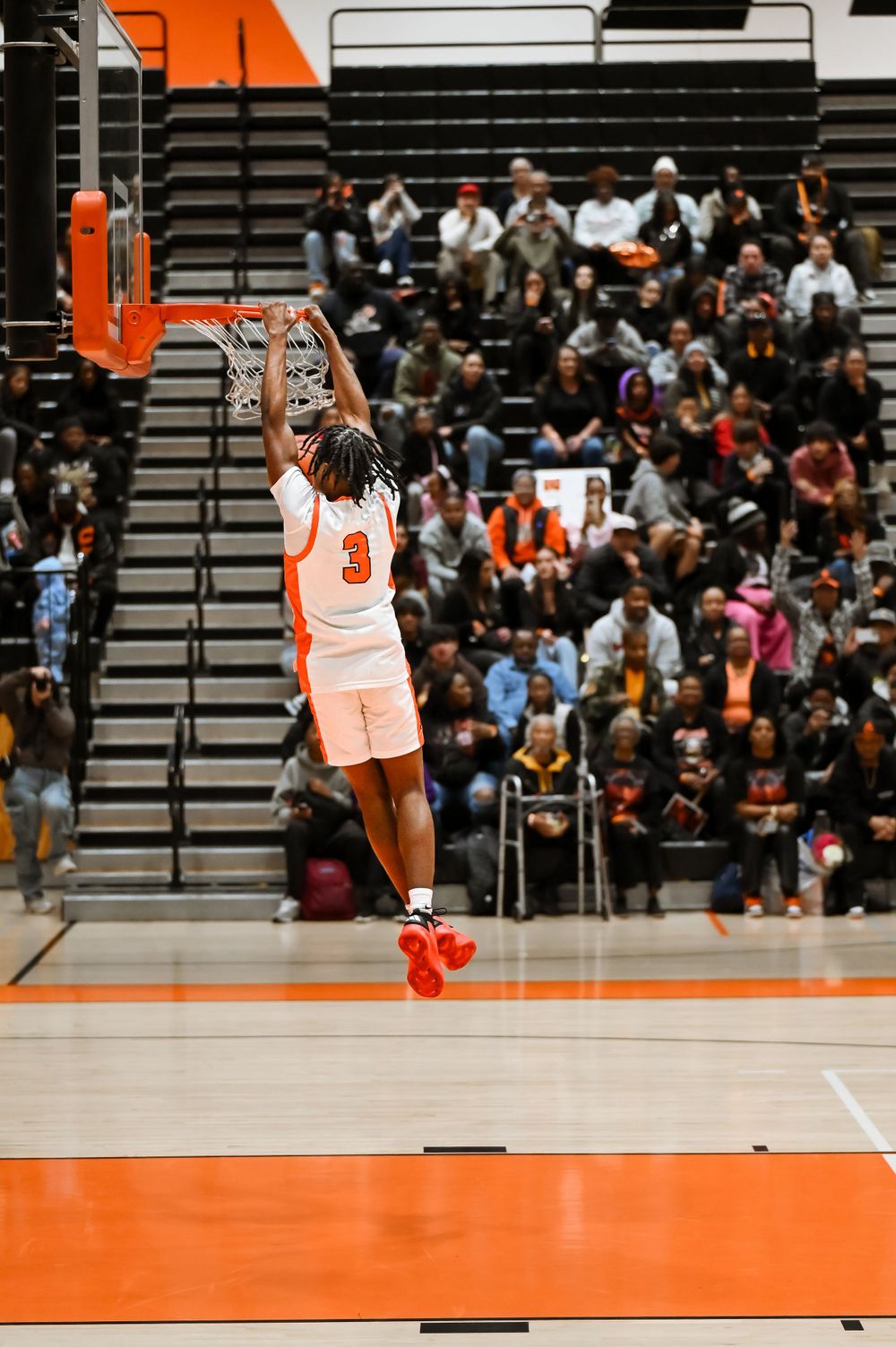Basketball players in orange and white uniforms leap high during a game on their home court.