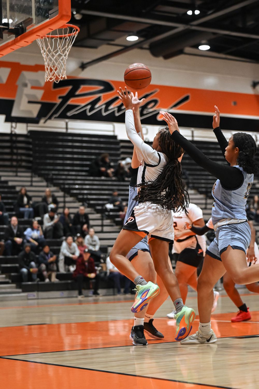 Players jump for a rebound under the basketball hoop during an intense game moment.