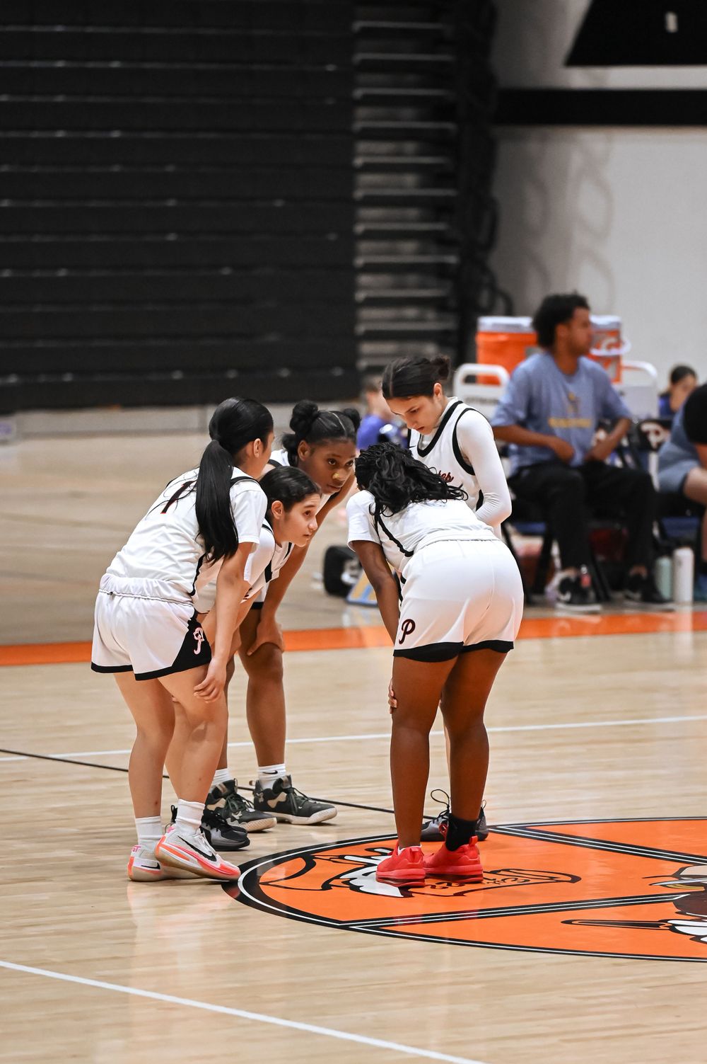 Basketball players huddle together on an orange court with black walls during a game.