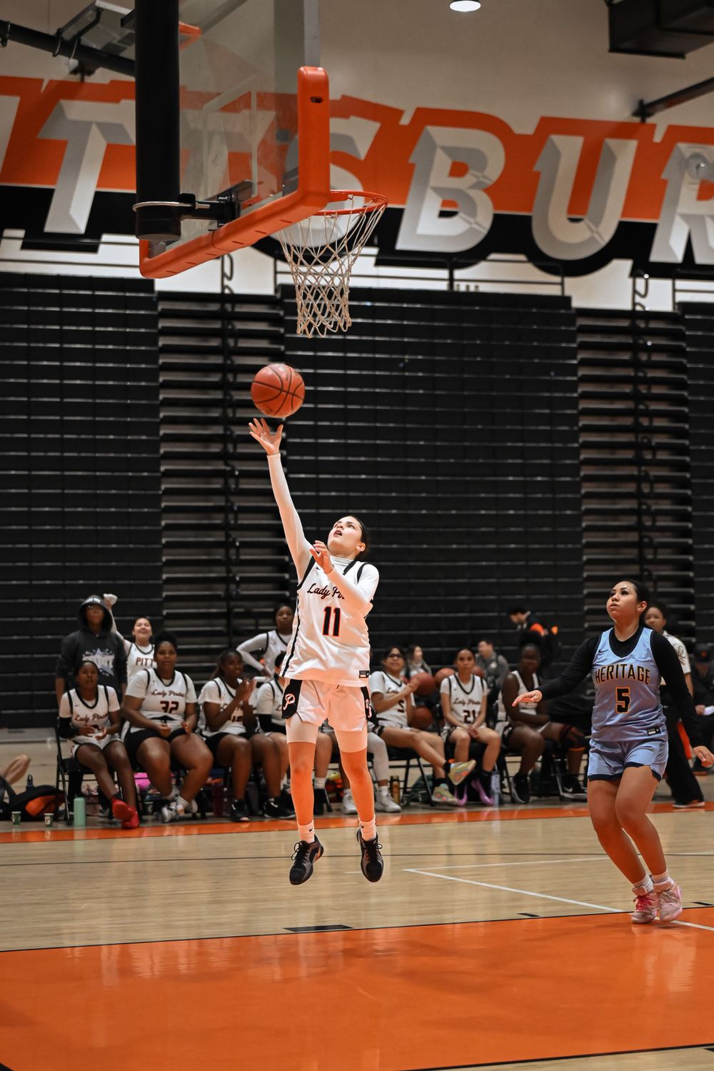 Basketball player leaps for a layup shot against a dark background with orange accents.