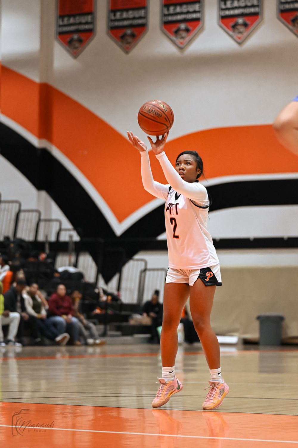 Basketball player takes a jump shot against orange and black backdrop with league banners.