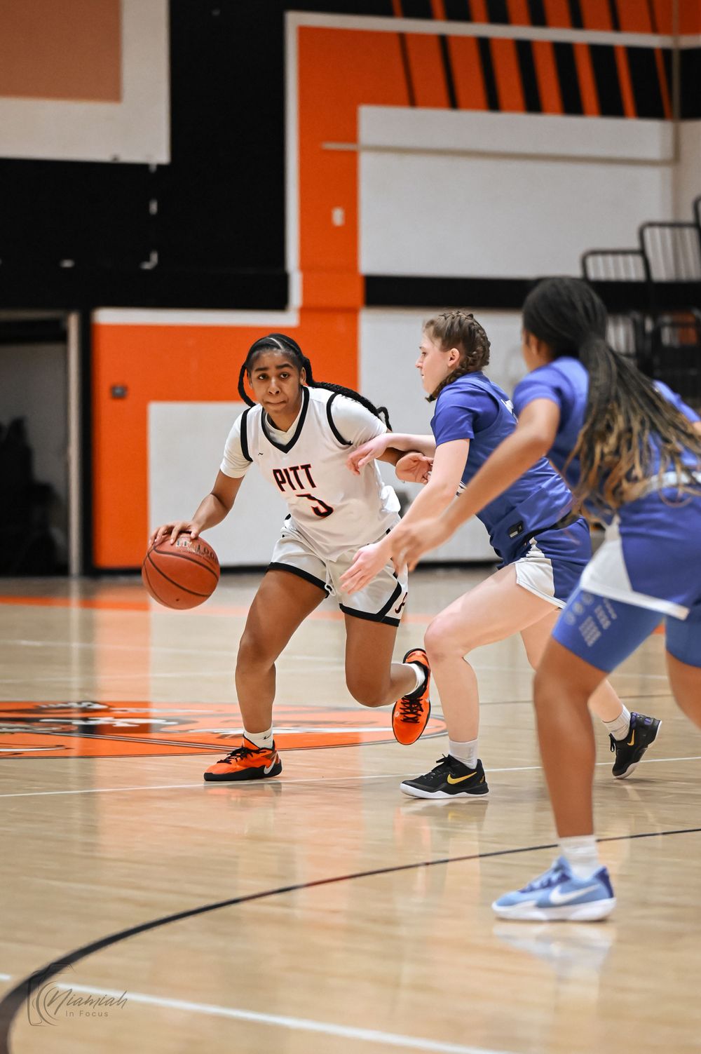 Basketball player dribbles past defenders during competitive game on orange court.