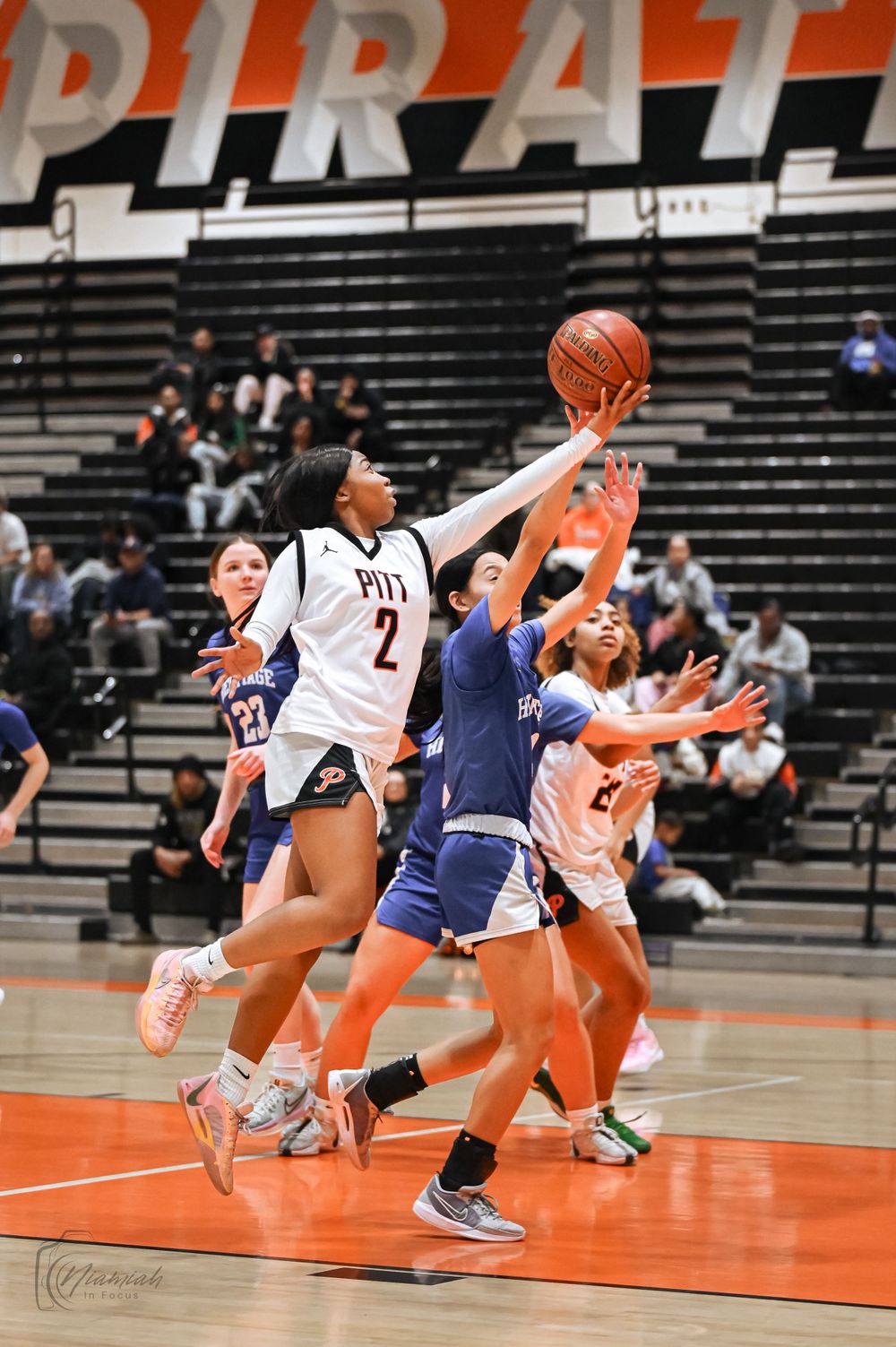 Players battle for possession during basketball game with PIRATE text visible in background.