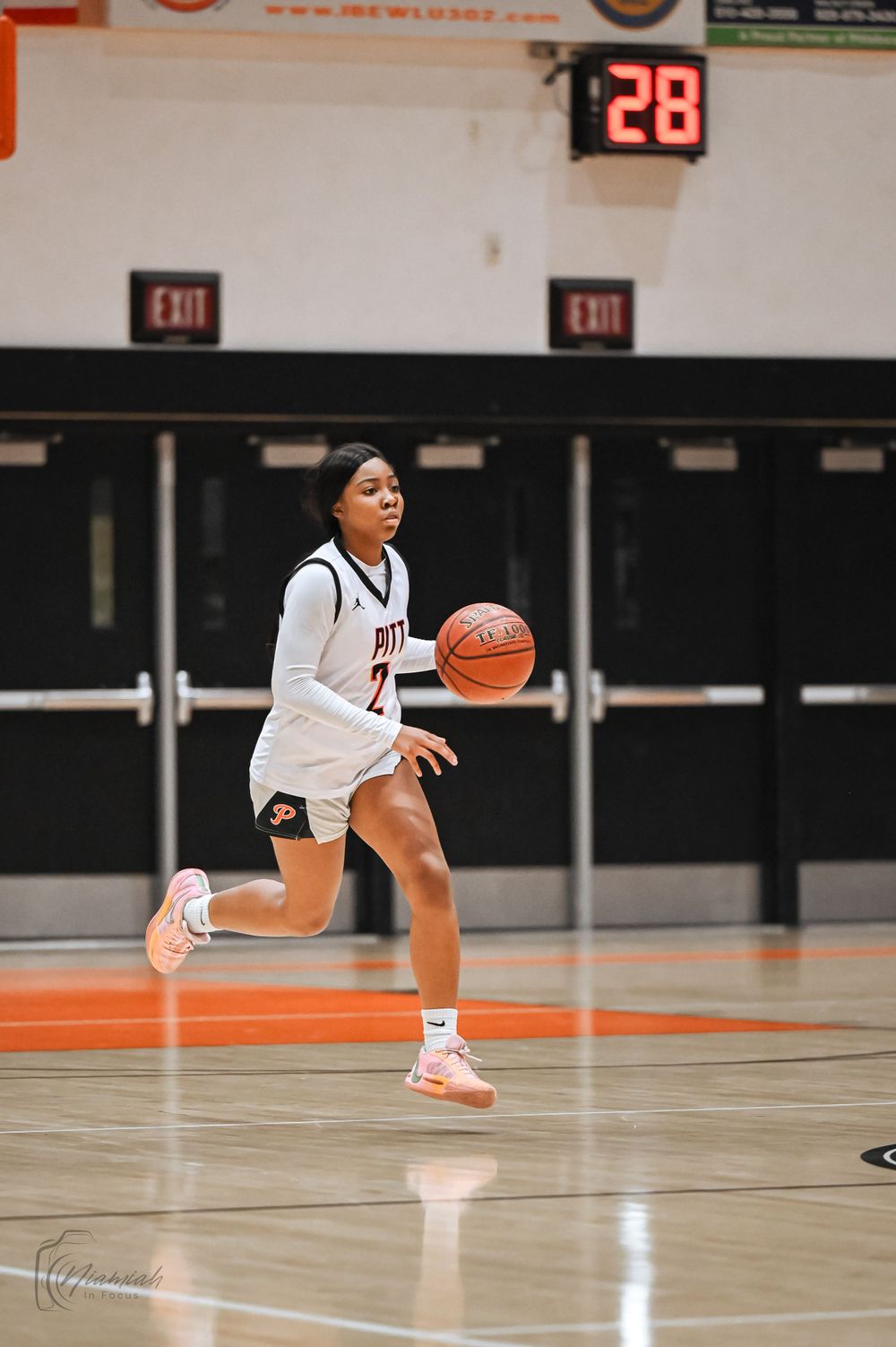 Basketball player dribbles on orange court with scoreboard showing 28 in background.