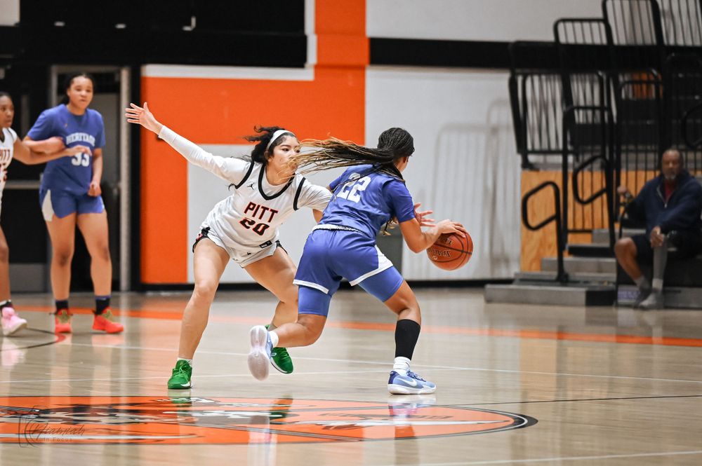 Basketball players in blue and white uniforms compete for the ball on an orange court during a game.