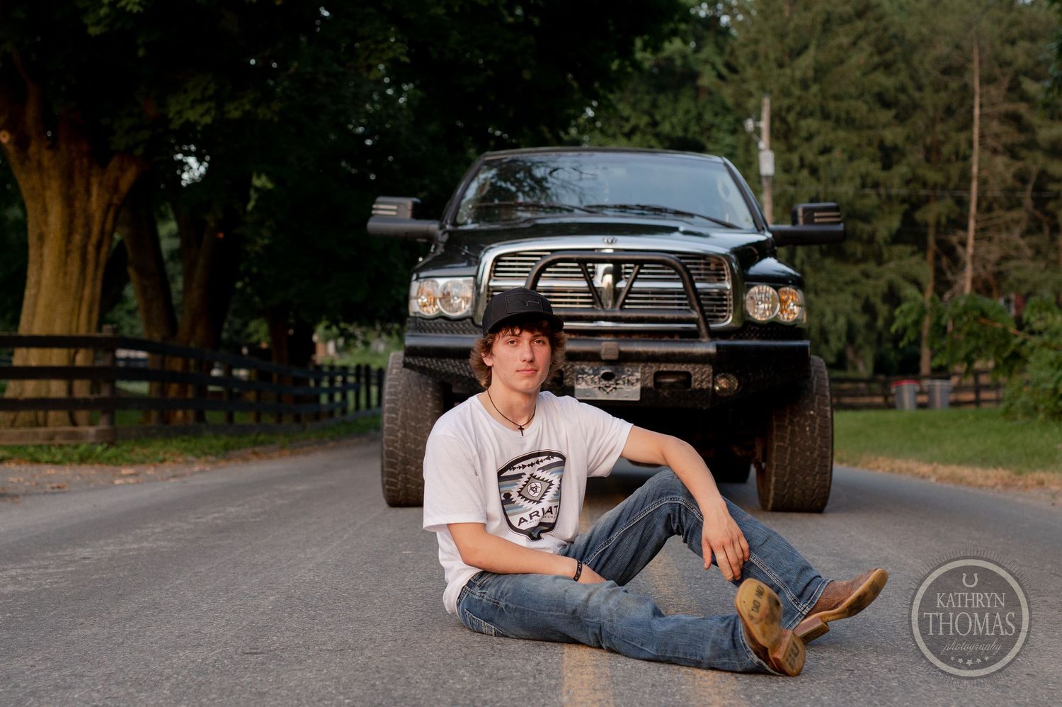 Customized black Dodge Ram with lift kit parked on rural road during sunset.