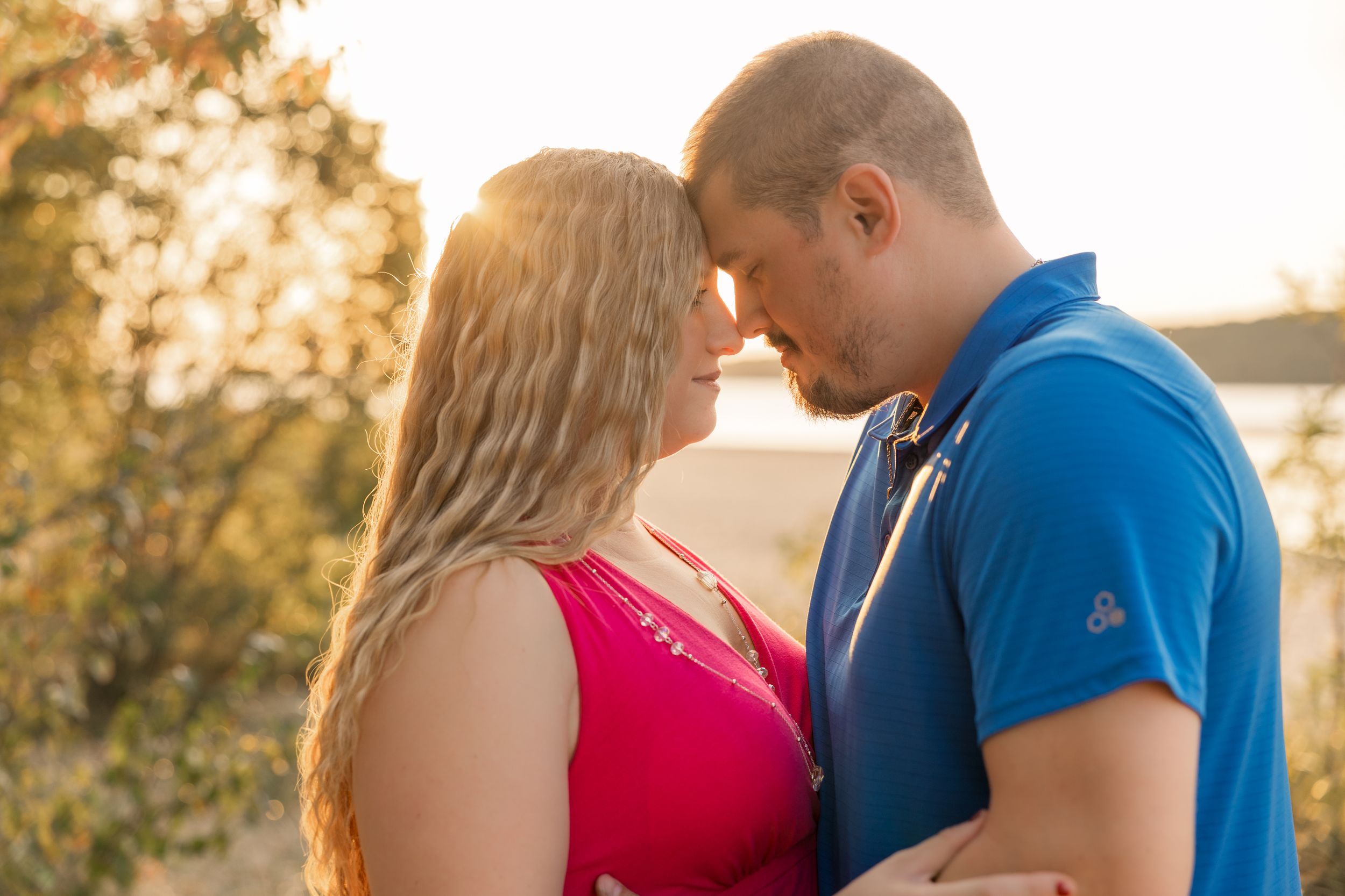 A couple shares an intimate moment at sunset as they stand close together wearing red and blue outfits.