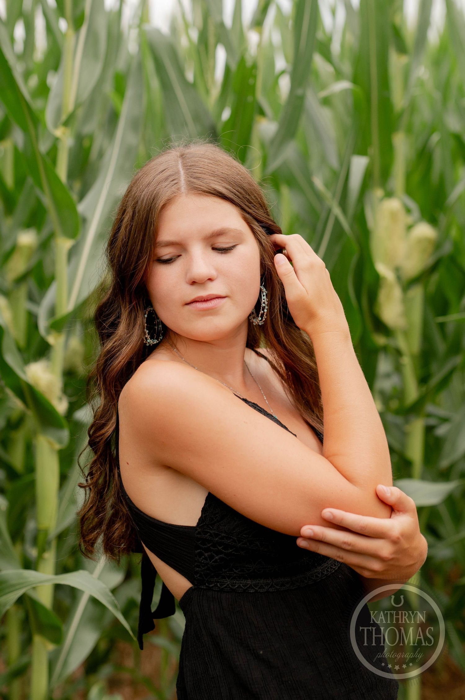 Woman in black top poses with closed eyes against backdrop of corn stalks.