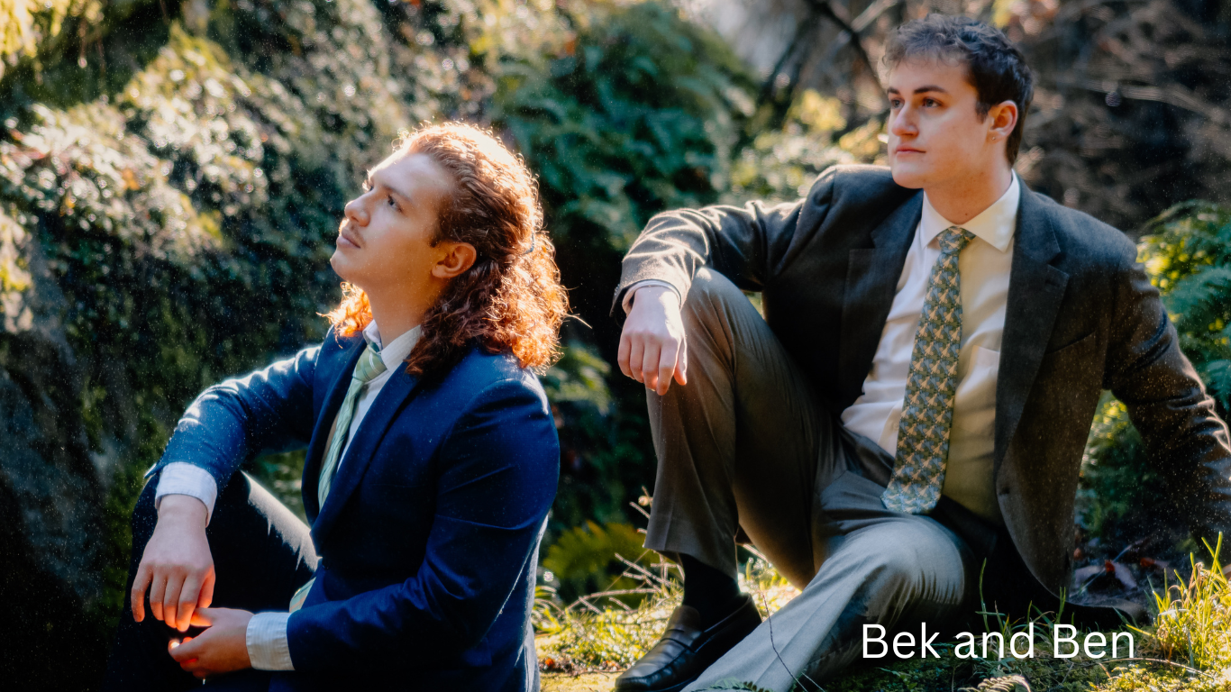 Two figures in professional attire sit outdoors among foliage in a candid moment.