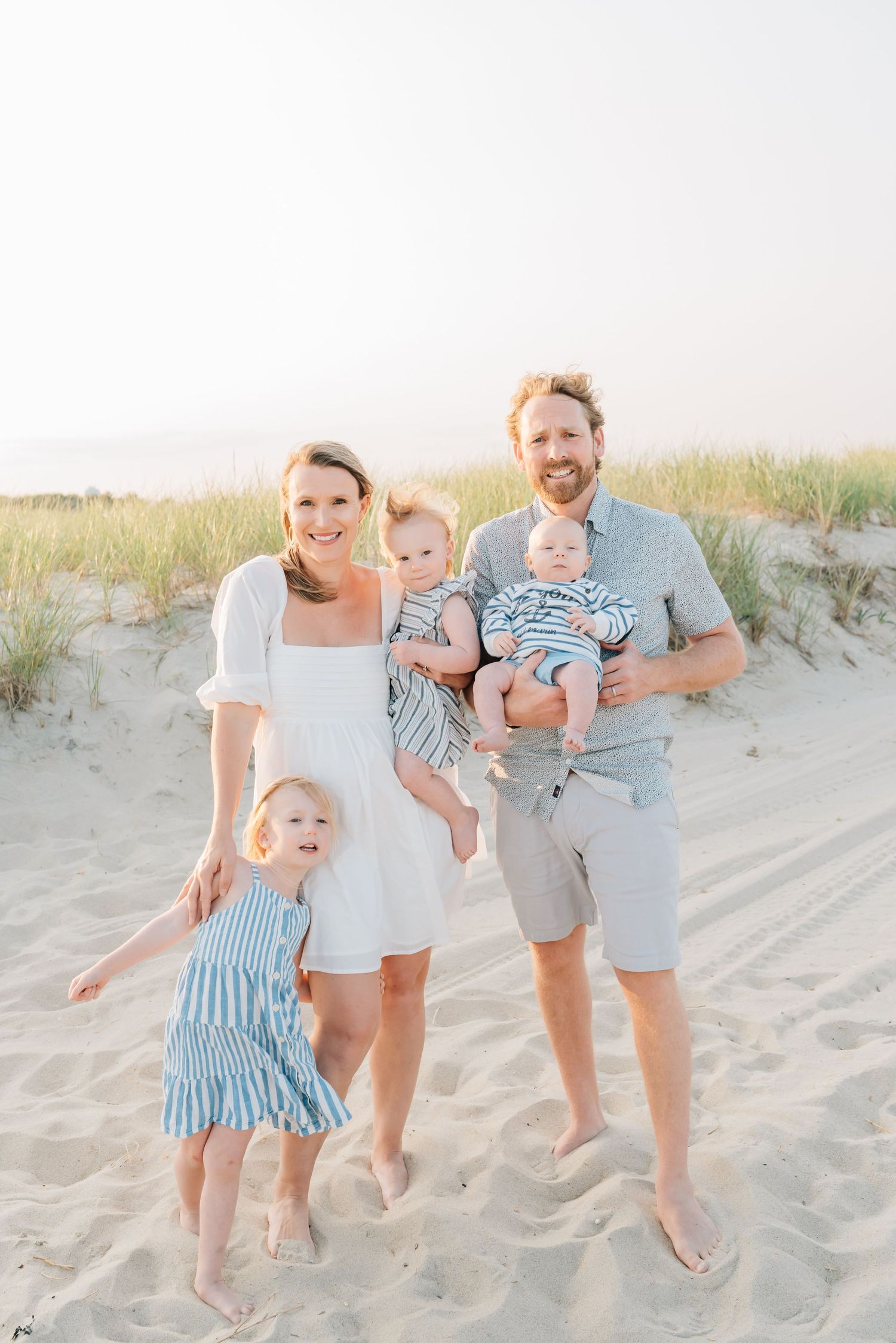 Parents holding their children, standing barefoot on the sand in Monmouth County, NJ.