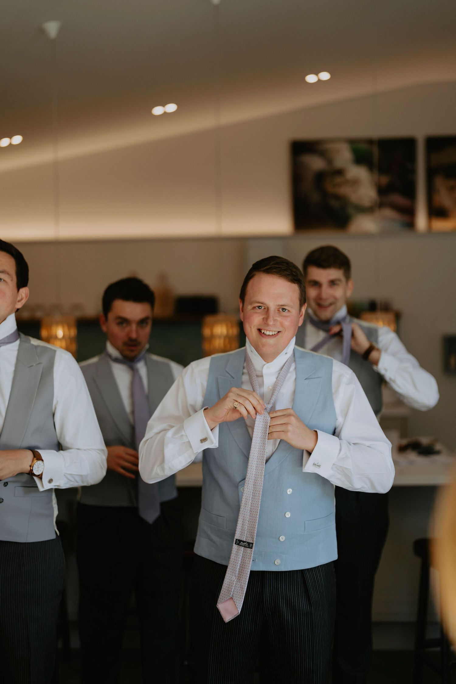 Groomsmen in formal attire getting dressed and adjusting their ties before a wedding ceremony in an elegant indoor setting.