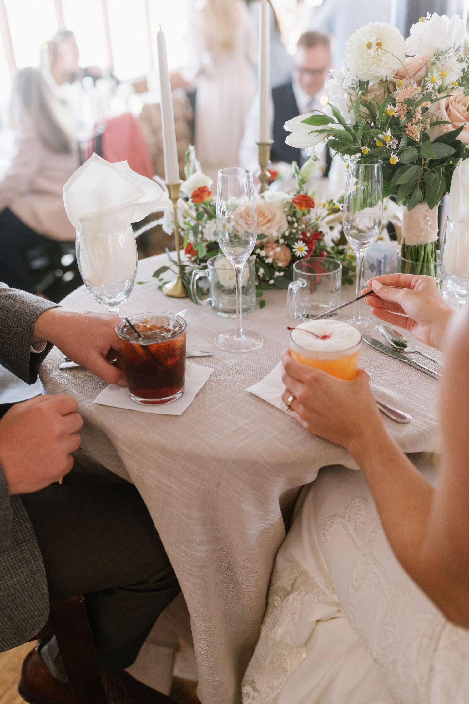 Elegant wedding reception table with drinks, floral centerpieces and place settings.