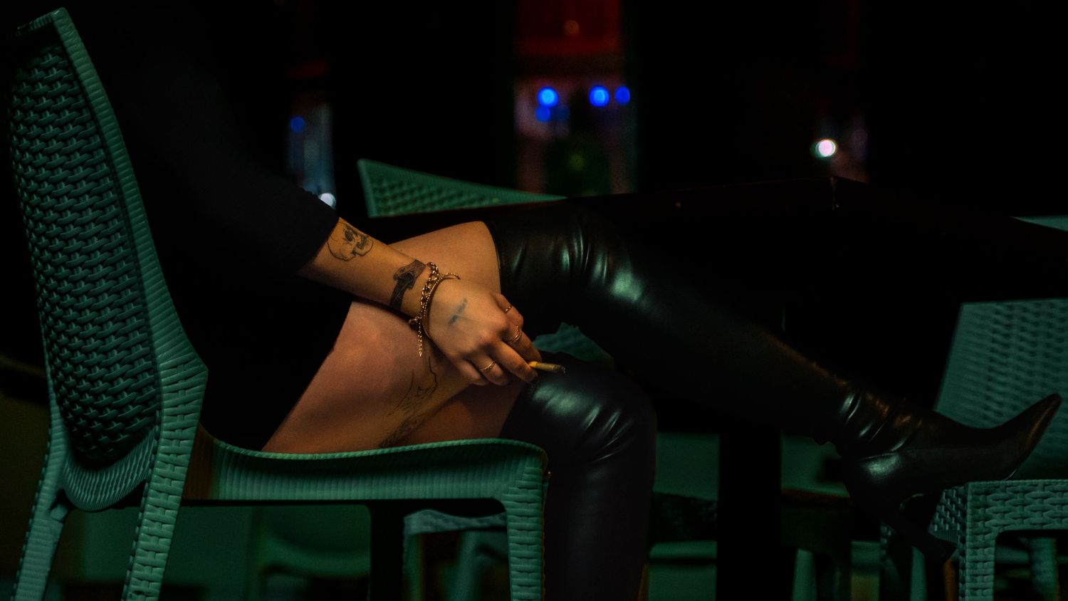A hand holds a microphone against a dark background with green chairs and dim lighting visible.