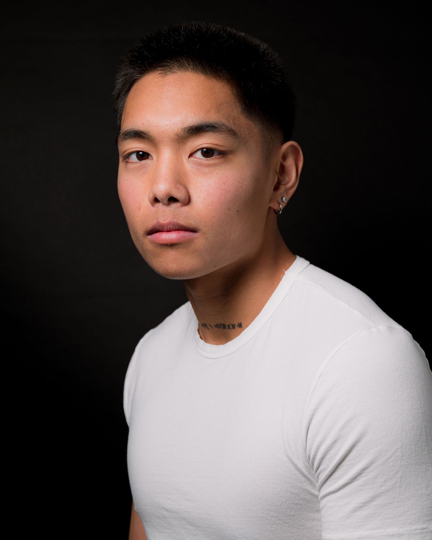 Clean professional headshot in white t-shirt against dark background.