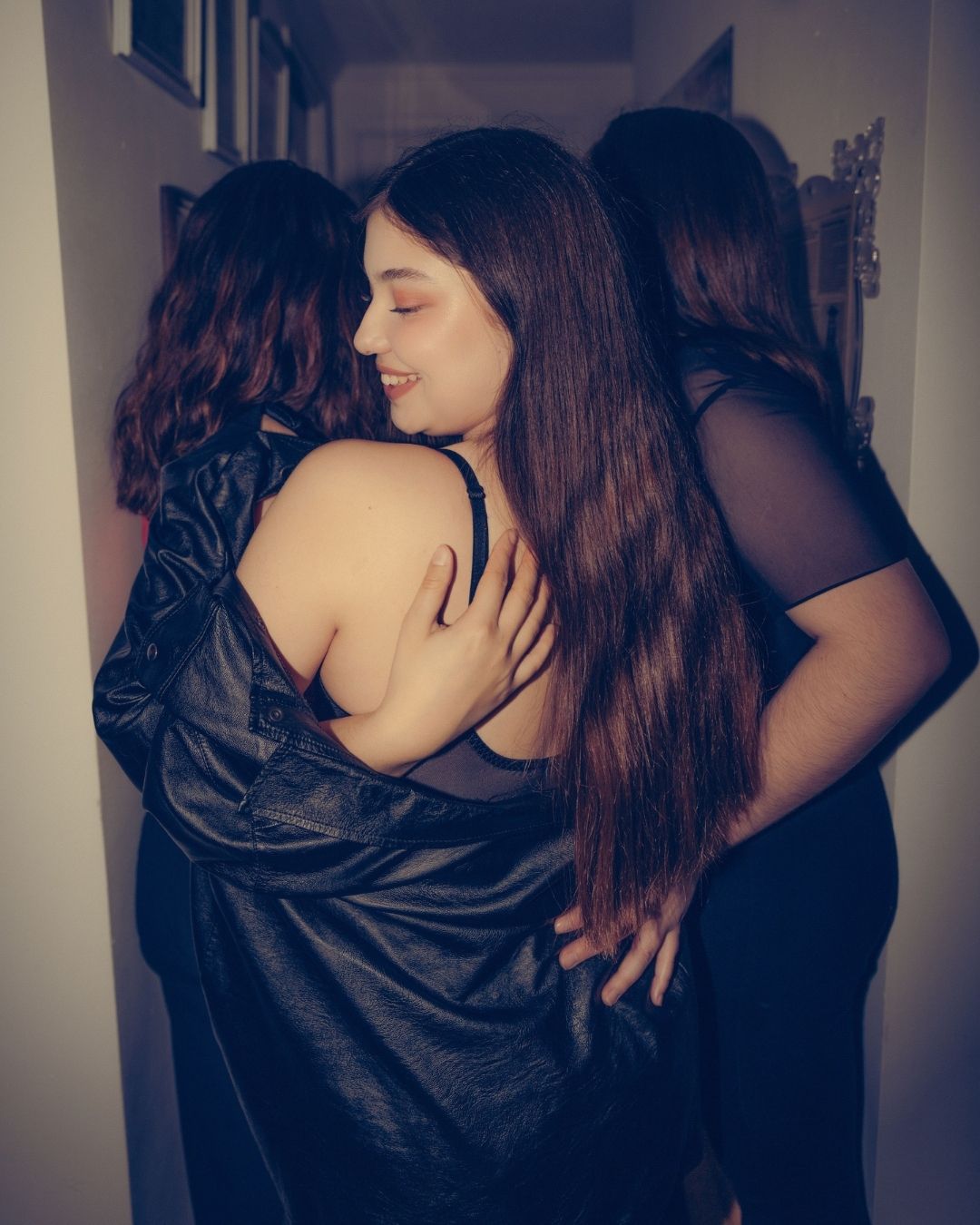 Two women sharing a warm embrace in a hallway at an indoor gathering.
