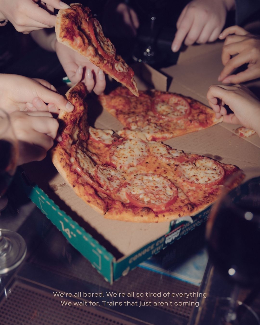 Friends sharing a pizza from a Dominos box, reaching for slices together at a casual gathering.