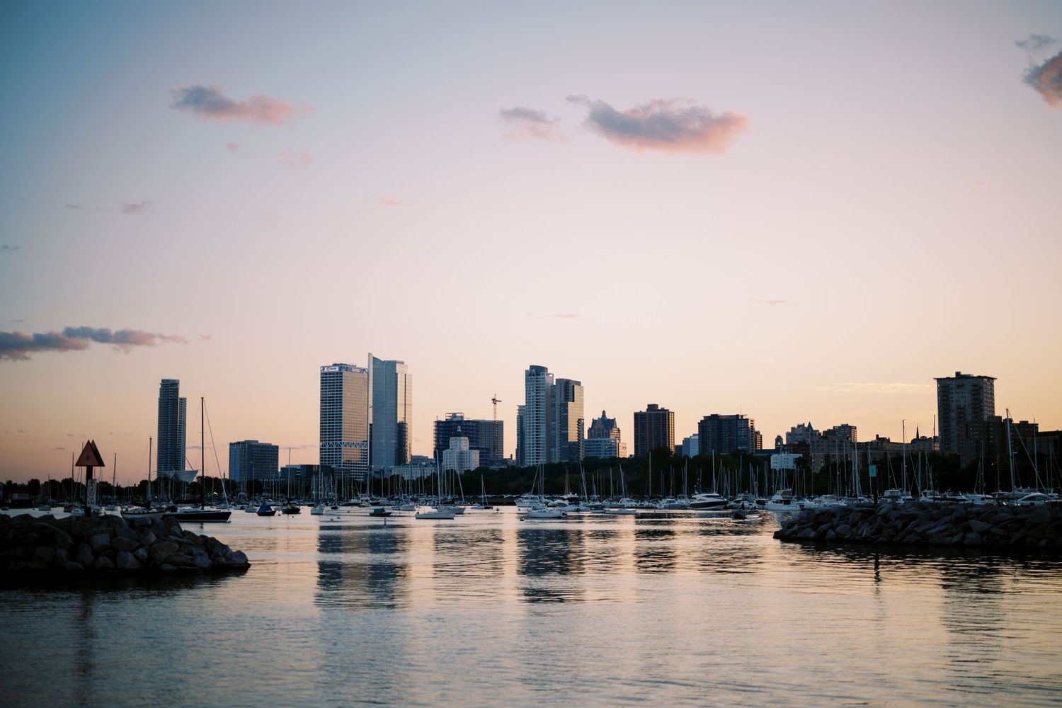 Boston skyline silhouetted against pink sunset sky with Charles River reflections in the foreground.