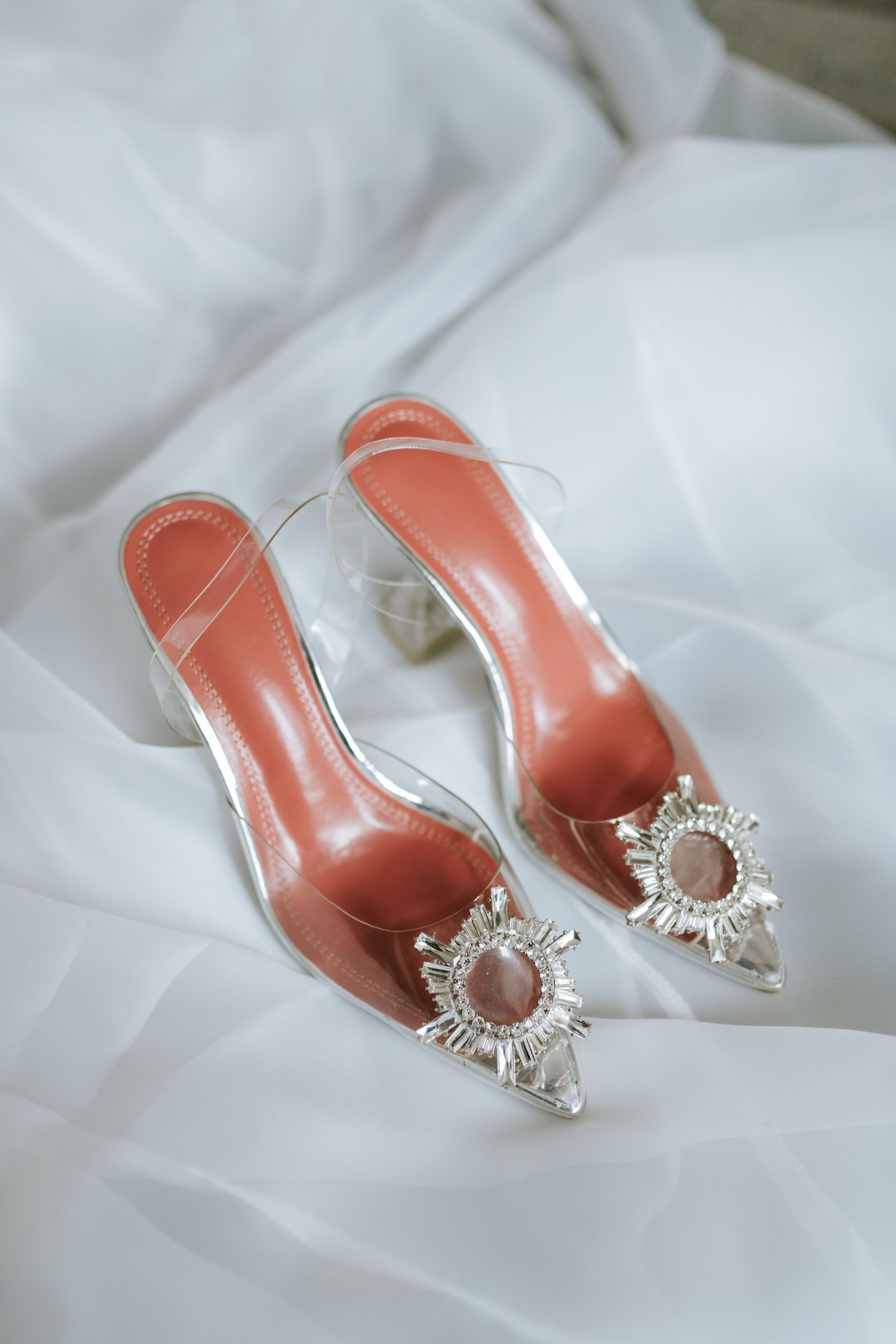 Elegant pink pointed-toe heels with crystal embellishments on white fabric.