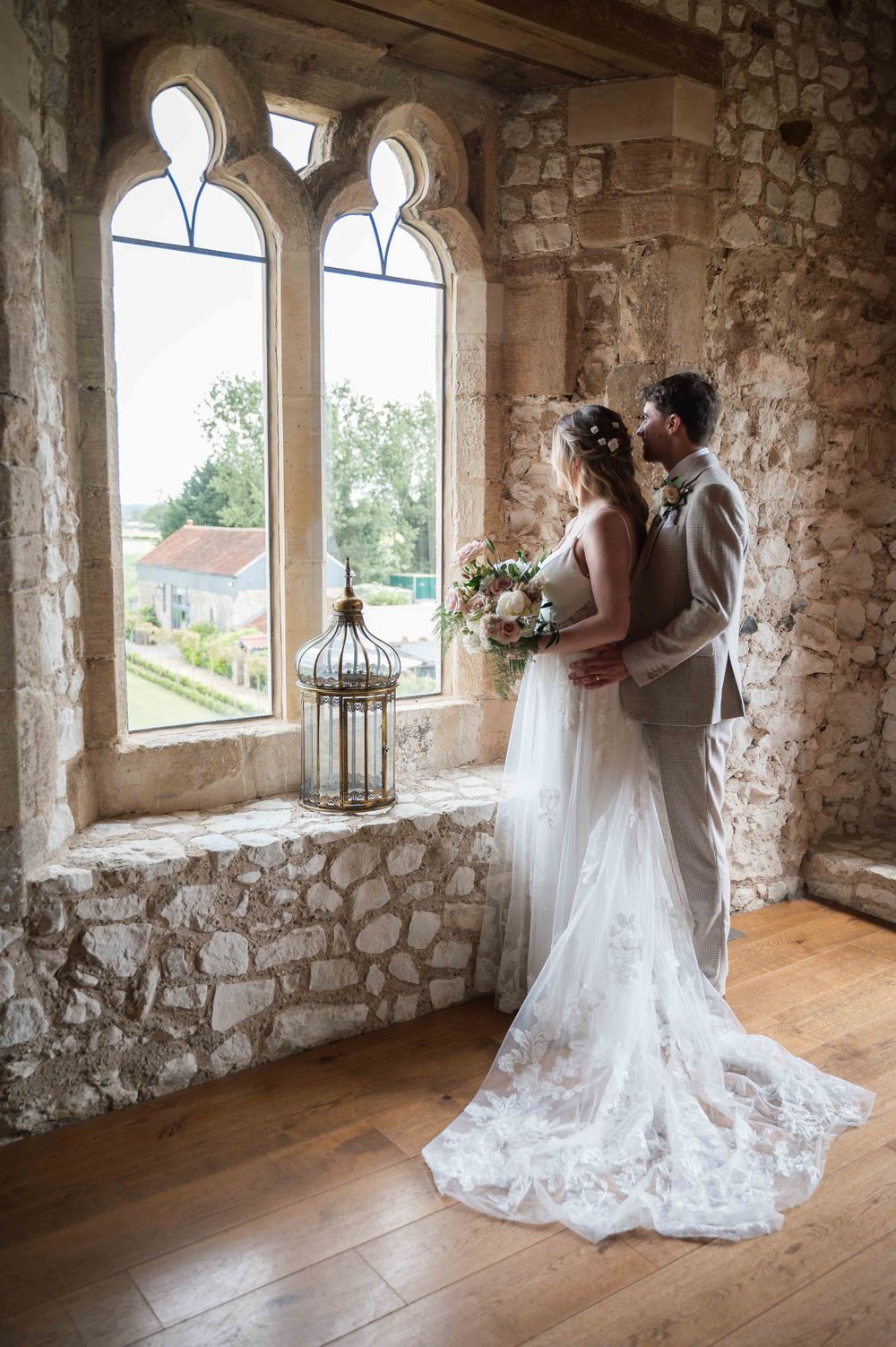 A romantic wedding scene in a medieval stone castle window alcove with gothic arches and a decorative lantern.