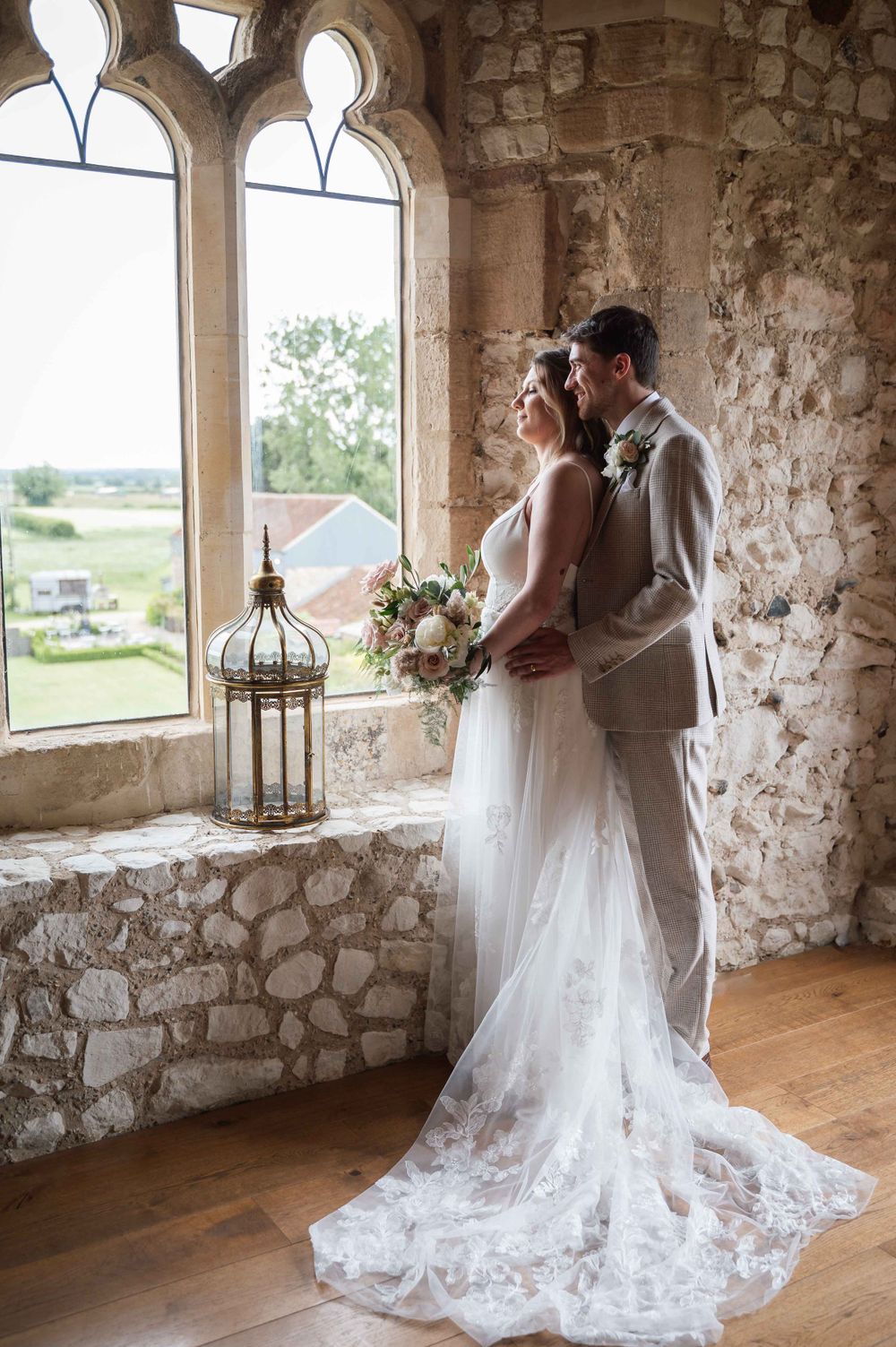A romantic wedding moment captured by a stone window in a rustic castle setting with scenic countryside views.